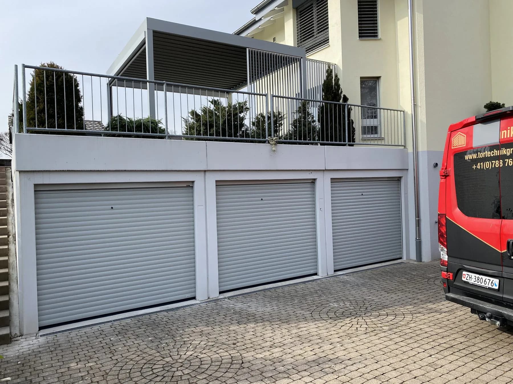 Drei helle Rolltore an einer Garagenzeile unter einer Terrasse