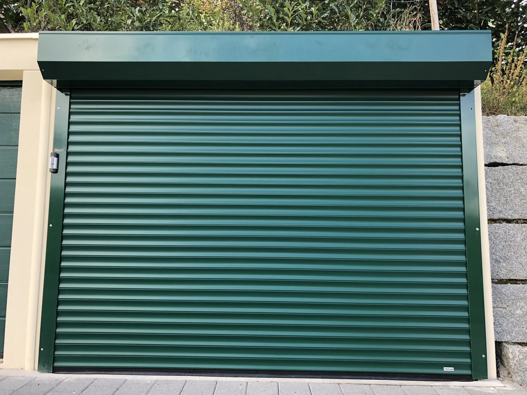 Gruenes Rolltor an einer Garage vor einer Natursteinmauer