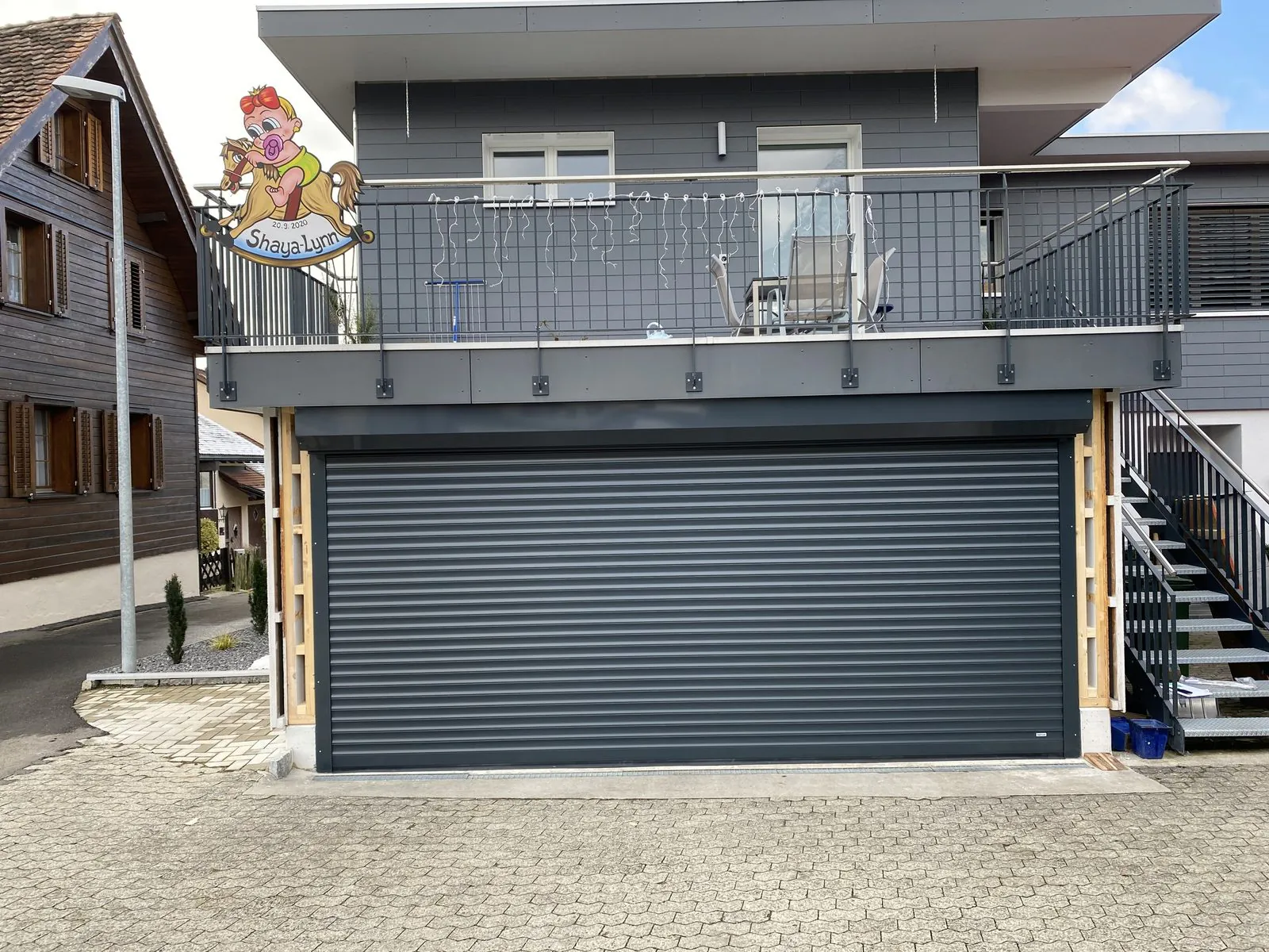 Anthrazitfarbenes Rolltor an einem Mehrfamilienhaus mit Holzverkleidung